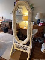 Full view of white wicker dressing mirror standing upright in living room with octagonal shape and woven wicker frame.