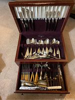 Full view of the wooden flatware case with upper and lower compartments displaying assorted knives, forks, spoons, and specialty utensils.