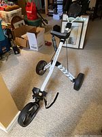 Full view of the white Tourtrek folding golf cart showing three wheels and black grips, folded open standing on carpet indoors.