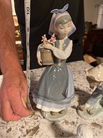 Lladro girl figurine with detailed blue dress and flowers, measured with tape showing about 10 inches tall.