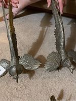 Photo displaying two heavy metal fighting bird sculptures held by hands, showing detailed feathers and long tails