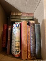 Box of 9 assorted old hardcover books with worn cloth bindings, some with decorative gold embossing, one with torn dust jacket