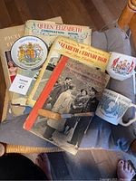 Full view of all items in the lot including the books, cups, saucer, and cutting tool placed together on a chair.