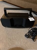 Front view of black portable satellite radio boom box placed on carpet with power adapter cables alongside.