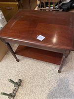 Full view of the wooden side table showing the top surface, turned legs, and lower shelf. The wood finish is dark with some worn areas.