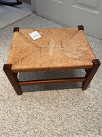 Top view of a rectangular twine footstool showing water damaged areas on the woven seat and wooden frame legs.
