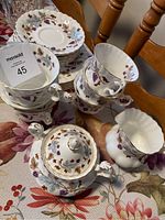 Tea cups stacked with matching saucers and dessert plates, showing gold-trimmed edges and floral grapevine pattern.