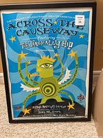 Full front view of framed blue concert poster for The Tragically Hip and guests, text and graphics visible.