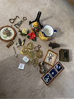 Overview of all items spread on carpet including horse brasses, pottery jug, binoculars, small framed art, figurines, small metal tools and other trinkets.