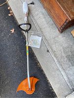 Full view of Stihl FSE 60 electric weed wacker with orange cutting guard and replacement line in plastic bag.