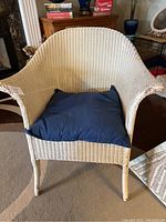 Front view of the white wicker chair with blue pillow on the seat, showing overall chair shape and condition.