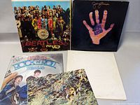 Four vinyl record albums laid out, showing covers including The Beatles Sgt. Pepper's Lonely Hearts Club Band and George Harrison albums.