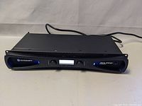 Front view of black Crown amplifier showing full front panel with Crown logo, dual knobs and unlit LCD