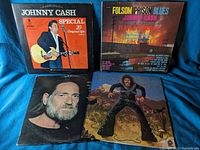 Four country music vinyl records, front covers visible showing Johnny Cash and Willie Nelson albums with some wear and scratches.