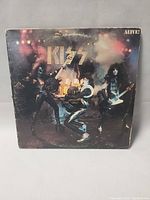 Front cover of Kiss Alive! album featuring band performing on stage with 'ALIVE!' text visible