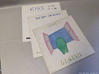 Three vinyl records stacked with visible covers: KISS live recordings, Bob Dylan Life Sentence, and Genesis Duke album.
