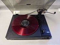 Full view of Nikko NP100 turntable with red translucent vinyl record on platter, lid open.