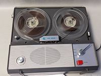 Front view of Sears tape recorder showing tape reels turning, speaker grill, and control panel with lever and record button.