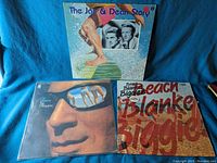Three surf music vinyl albums: The Jan & Dean Story, Girl Watcher by The O'Kaysions, Beach Blankies by Beach Blankies.