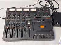 Front angled view of recorder showing faders, knobs, meters, cassette door and attached power supply brick