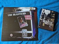Photo showing the vinyl album cover of The Blasters Over There Live At The Marquee London and the DVD of The Blasters Live Going Home on a blue fabric background.