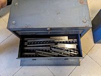 Open metal toolbox showing bottom drawer with multiple precision gauge blocks of various sizes