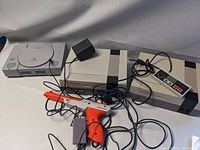 Nintendo Entertainment System (NES) console with wired controller and orange light gun, also power adapter visible