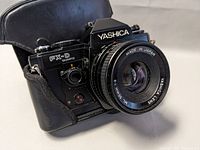 Photo showing Yashica FX-D quartz SLR camera with attached Yashica ML 50mm f/2 lens in a black protective case.