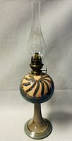 Full view of vintage pottery hurricane lamp showing bulbous pottery design with beige and blue swirls, brass burner, and clear glass chimney