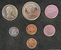 Close-up of all 7 coins arranged on black felt showing detail of Queen Elizabeth II profiles and Canadian motifs such as maple leaf, beaver, caribou, Bluenose schooner.