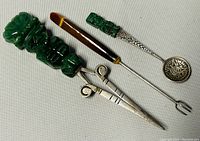 Three vintage utensils with carved green tribal handles showing Aztec Mayan patterns, including a spoon, fork, and pointed tool.