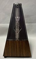 Front view of the vintage Wittner metronome showing the clear plastic upper case, visible pendulum, tempo scale, and faux wood finish on the base.