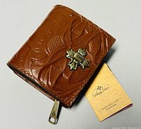 Brown tooled leather wallet with brass clasp and original tag laying on a white background