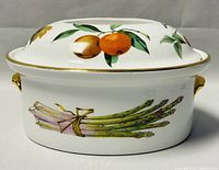 Front view of Royal Worcester Evesham oval covered casserole dish showing asparagus and orange designs with gold edge.