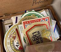 View inside wooden humidor box containing assorted vintage beer bottle labels stacked and spread out, showcasing brand logos and colors.