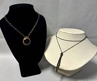 Two copper necklaces displayed on black and white busts, showing the difference in pendant shapes and chain lengths.