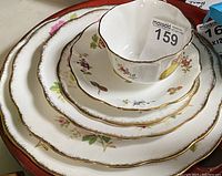 Stacked view of four plates with scalloped gold edges and floral-fruit pattern, topped with teacup and saucer.