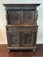 Front view of the entire oak cabinet showing two upper doors, a middle drawer section, and two larger bottom doors with detailed carvings.