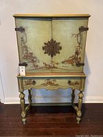 Front view of the two-tier jade green painted cabinet with decorative floral and landscape chinoiserie scenes and central metal hardware