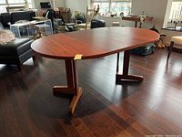 3/4 view of extended oval table showing teak finish and dual pedestal base