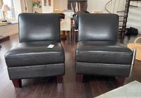 Front view of two black faux leather armless accent chairs with wooden block legs