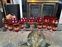Full set of red and gold-trimmed glasses arranged on glass table