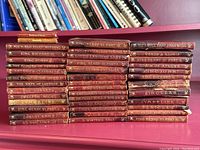 Three stacks of red leather bound volumes on a pink shelf