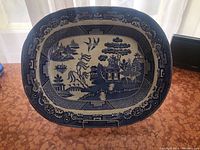 Full view of the large blue and white Blue Willow platter on stand, showing overall design and shape.
