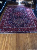Full view of antique Persian rug showing central geometric medallion design and border pattern in red, blue, and green colors laid on hardwood floor.