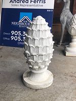 Front left angle view of the white resin artichoke finial showing textured surface and base with visible paint wear and crack.