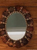 Full view of the seashell mirror showing the oval reflective glass framed by large scallop shells and smaller spiral shells around the perimeter.
