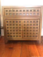 Full frontal view of one solid wood side table showing woven panel design and brass hardware