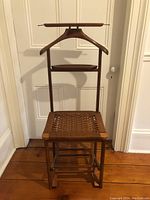 Full view of the walnut valet chair showing woven seat with visible wood frame, back wooden coat hanger, pants rack bar, and accessory shelf below the hanger.