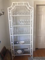 Front view of one white faux bamboo metal etagere fully loaded with glassware